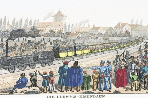 Eine Gruppe von Menschen, die um und in der Nähe eines Zuges auf einem Gleis stehen, mit einigen, die im Zug sitzen und anderen auf dem Boden, vor Gebäuden und Bäumen im Hintergrund, mit Text unten, der "Ludwigs-Eisenbahn, der erste Bahnhof in Deutschland" lautet.
