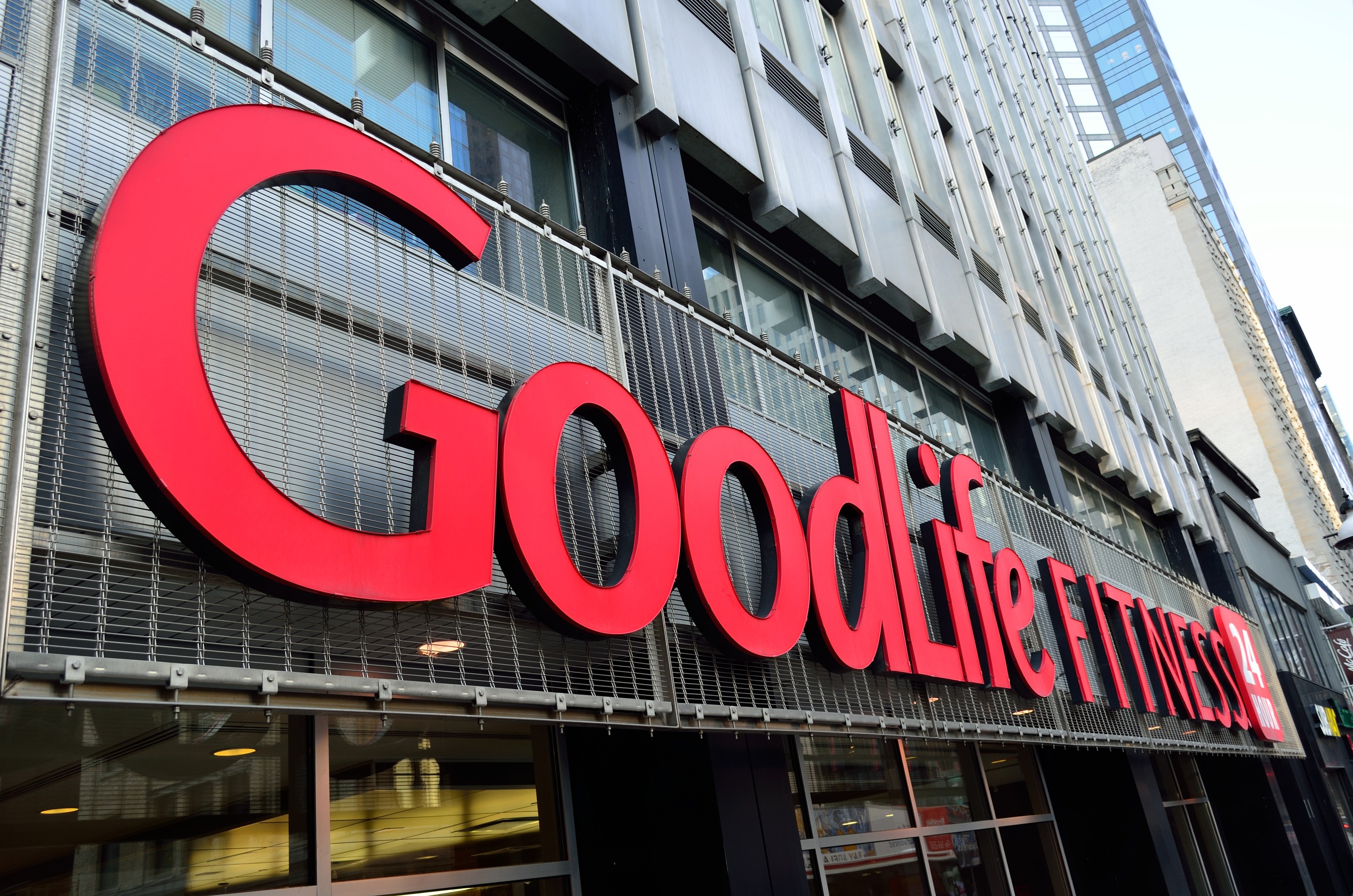 Außenansicht eines Goodlife Fitness Studios in New York City mit Glaswänden, einem Namensschild, benachbarten Gebäuden und dem Himmel im Hintergrund.