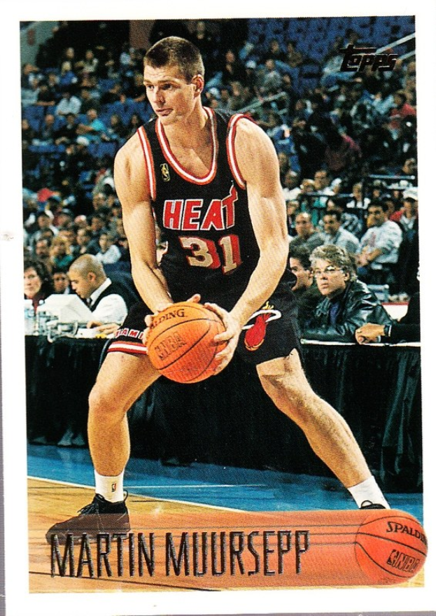 Ein Schwarz-Weiß-Foto von Martin Muirsepp, einem ehemaligen Spieler der Miami Heat, der einen Basketball hält, mit Menschen auf Stühlen und einem Tisch mit Gegenständen im Hintergrund, beschriftet mit "1991-92 Topps Basketball Card" unten.