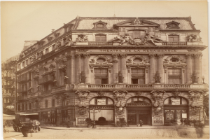 Altes Foto des Théâtre de la Renaissance in Paris mit seiner prunkvollen Fassade mit Fenstern, Säulen, Bögen und Skulpturen, mit einigen Menschen und Fahrzeugen im Vordergrund und dem Himmel im Hintergrund.
