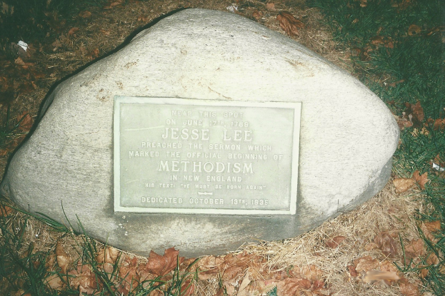 Ein großer Felsen mit einer Tafel, auf der 'Jesse Lee Methodism' steht, in einer grasbewachsenen Fläche umgeben von trockenen Blättern und Gras.