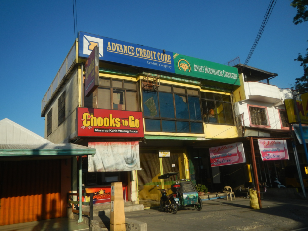 Ein Geschäftsgebäude mit einer Tafel, auf der "Advance Credit Corp" steht, auf einer Straße mit Fahrzeugen, Strommasten und Bäumen unter einem klaren Himmel.