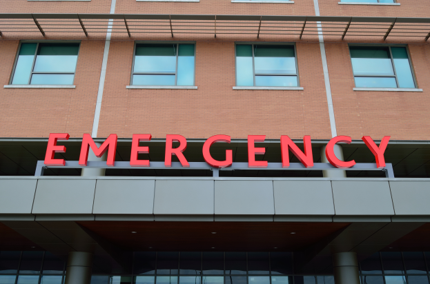 Ein Gebäude mit Glasfenstern, Säulen und einem sichtbaren roten Notfallzeichen, das darauf hinweist, dass es eine Notaufnahme ist.