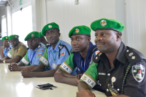 Eine Gruppe von Polizeibeamten sitzt an einem Tisch während einer Schulung, mit Mobiltelefonen und anderen Gegenständen auf dem Tisch, in einem Raum mit Fenstern und Deckenbeleuchtung.