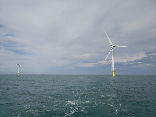 Drei Windräder im Meer mit bewölktem Himmel im Hintergrund, umgeben von der endlosen Weite des Meeres.