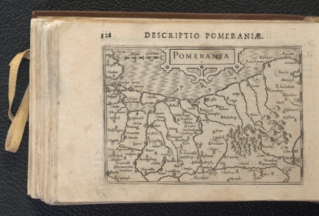 Ein altes Buch mit einer detaillierten Karte von Pommern auf einer schwarzen Oberfläche, das verschiedene Städte und Ortschaften zeigt.