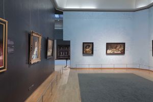 Ein prächtiger Raum in der Nationalgalerie in London, gefüllt mit zahlreichen Gemälden an den Wänden, Teppichboden, Geländern und einer Decke mit Beleuchtung.