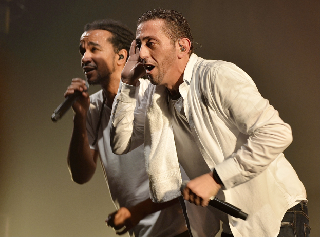 Zwei Männer in legerer Kleidung stehen nebeneinander auf der Bühne, jeder hält ein Mikrofon in der Hand.