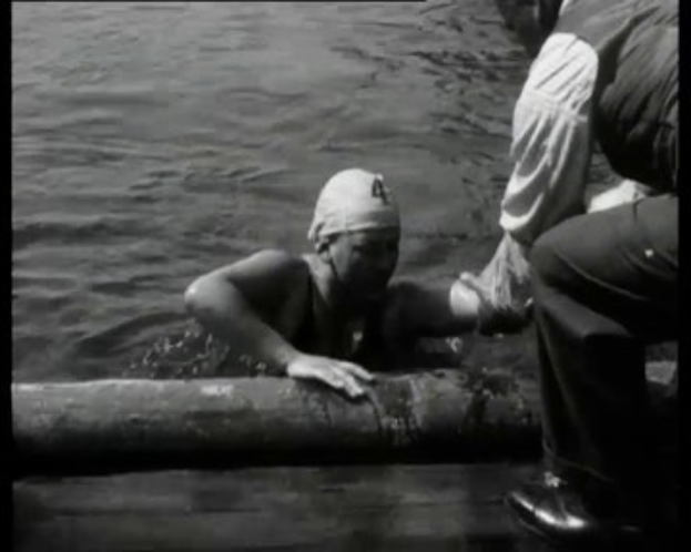 Schwarz-weißes Bild eines besorgten Mannes im Wasser mit einem Kopfverband, umgeben von zwei Personen auf der rechten Seite.