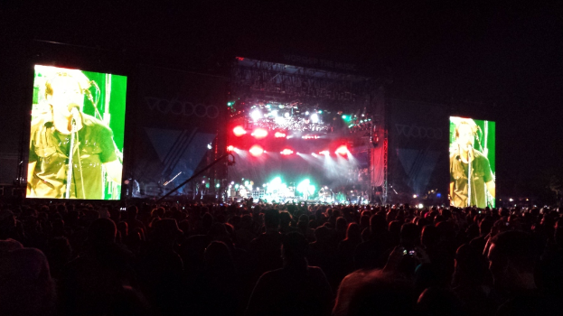 Eine Konzertszene mit einer Menge unten, einem großen Bildschirm links und einem kleineren rechts.