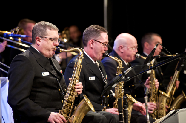 Eine Gruppe von Männern in Anzügen und Krawatten, die Saxophone auf der Bühne spielen, mit Mikrofonen im Vordergrund.