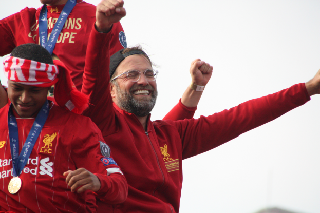 Liverpool-Trainer Jurgen Klopp feiert mit seinen Spielern den Sieg in der UEFA Champions League, umgeben von zwei medaillenbewehrten Personen und dem Himmel im Hintergrund.