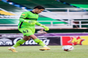 Ein Mann in einem grünen Torwarttrikot schießt einen Fußball auf einem Rasenfeld in einem Stadion, im Hintergrund sind Banner mit "Chivas USA vs Mexico City, 3-1, Copa Libertadores" zu sehen.
