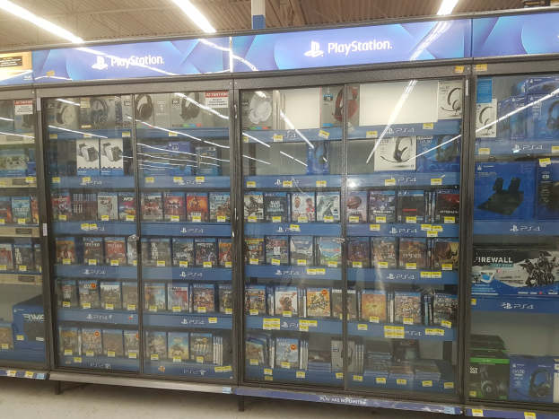 Ein PlayStation-Store-Innenraum mit Regalen voller Video-Spiele, die mit Preisschildern beschriftet sind, Deckenleuchten und einer "PlayStation Store"-Aufschrift oben.