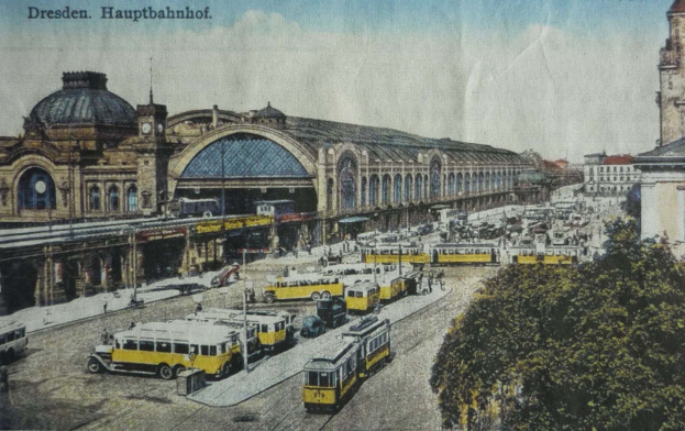 Eine sepiafarbene Vintage-Postkarte des Dresdner Hauptbahnhof Bahnhofs in Dresden, Deutschland, zeigt eine belebte Straßenszene mit Fahrzeugen, Fußgängern, Bäumen, Gebäuden und einem bewölkten Himmel.