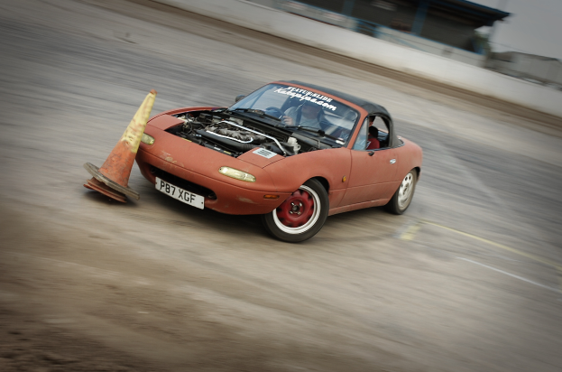 Eine Person fährt ein rotes Auto auf einer Rennstrecke, fahrt an einer Verkehrsüberwachung vorbei mit einem unscharfen Hintergrund, der hohe Geschwindigkeit andeutet.