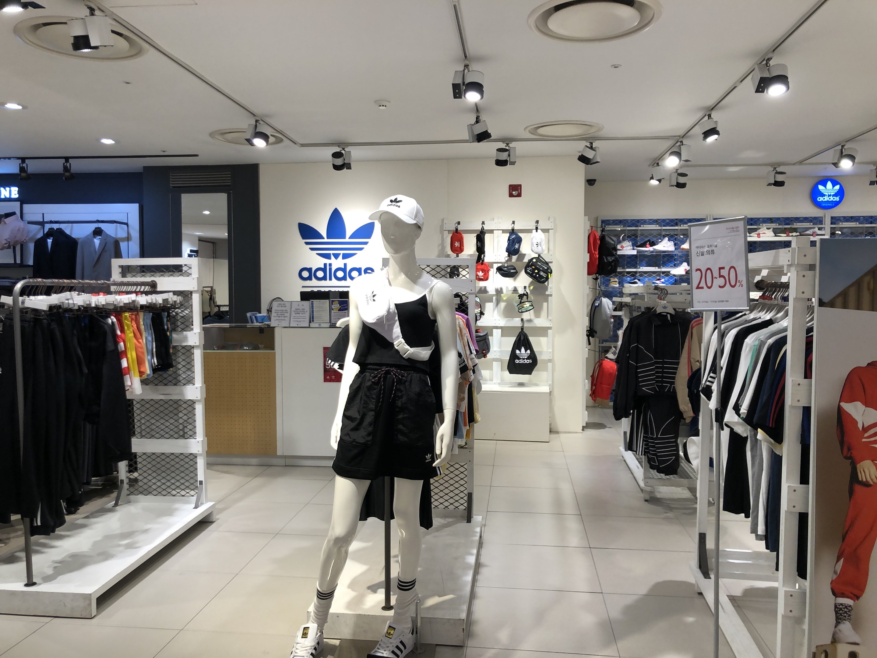 Innenansicht eines adidas-Geschäfts in Singapur mit Schaufensterpuppen, Kleiderständern, einer Texttafel auf der rechten Seite und Deckenleuchten.