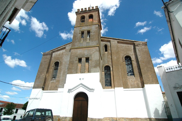 Gebäude dominieren das Bild, mit Autos und Bäumen im unteren linken Eck und einem bewölkten Himmel oben.