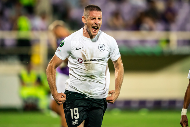 Ein Mann in weißem Hemd und schwarzen Shorts rennt auf einem Fußballfeld, umgeben von einer Gruppe von Menschen, die ein Tor feiern während eines Spiels zwischen Leeds United und Melbourne Victory.