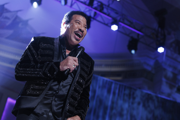 Lionel Richie performs auf den Grammys, trägt einen schwarzen Anzug und hält ein Mikrofon auf einer hell erleuchteten Bühne.