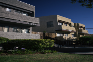 Eine Reihe von Wohngebäuden in San Francisco mit Fenstern, Pflanzen, Gras, einem Zaun, Treppen, einem Baum, Drähten und einem Himmel im Hintergrund.
