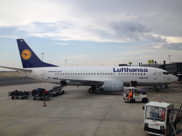 Ein Lufthansa Airbus A320-200 auf dem Frankfurt Airport geparkt, mit Bodenfahrzeugen, Wagen, Verkehrskegeln, Pfählen und Texttafeln im Bild.