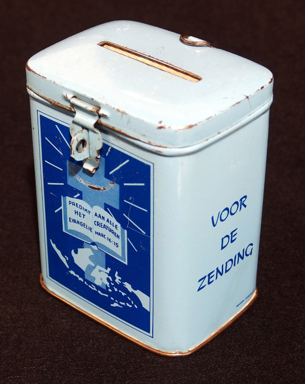 Weißer und blauer Blechspartopf mit einem blauen und weißen "Voor de Zending" Schild, auf einer schwarzen Oberfläche platziert.