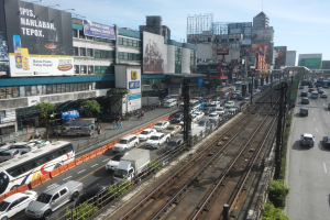Eine belebte Stadtstraße mit starkem Verkehr, Fußgängern, hohen Gebäuden und einem bewölkten Himmel im Hintergrund.