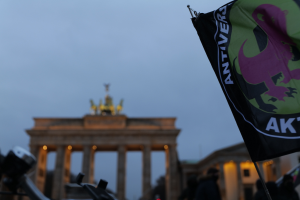 Eine Gruppe von Menschen steht vor dem Brandenburger Tor in Berlin, Deutschland, mit einer Fahnenstange, die ein Logo und Text trägt, und protestiert gegen die antifaschistische Bewegung.