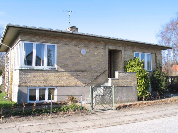 Zweizimmer-Detached-Bungalow mit Dach, Fenstern, Tür, Treppe, Metallzaun, Pflanzen, Gras, Bäumen, Satellitenschüssel und bewölktem Himmel in St Johns Wood, Swindon.