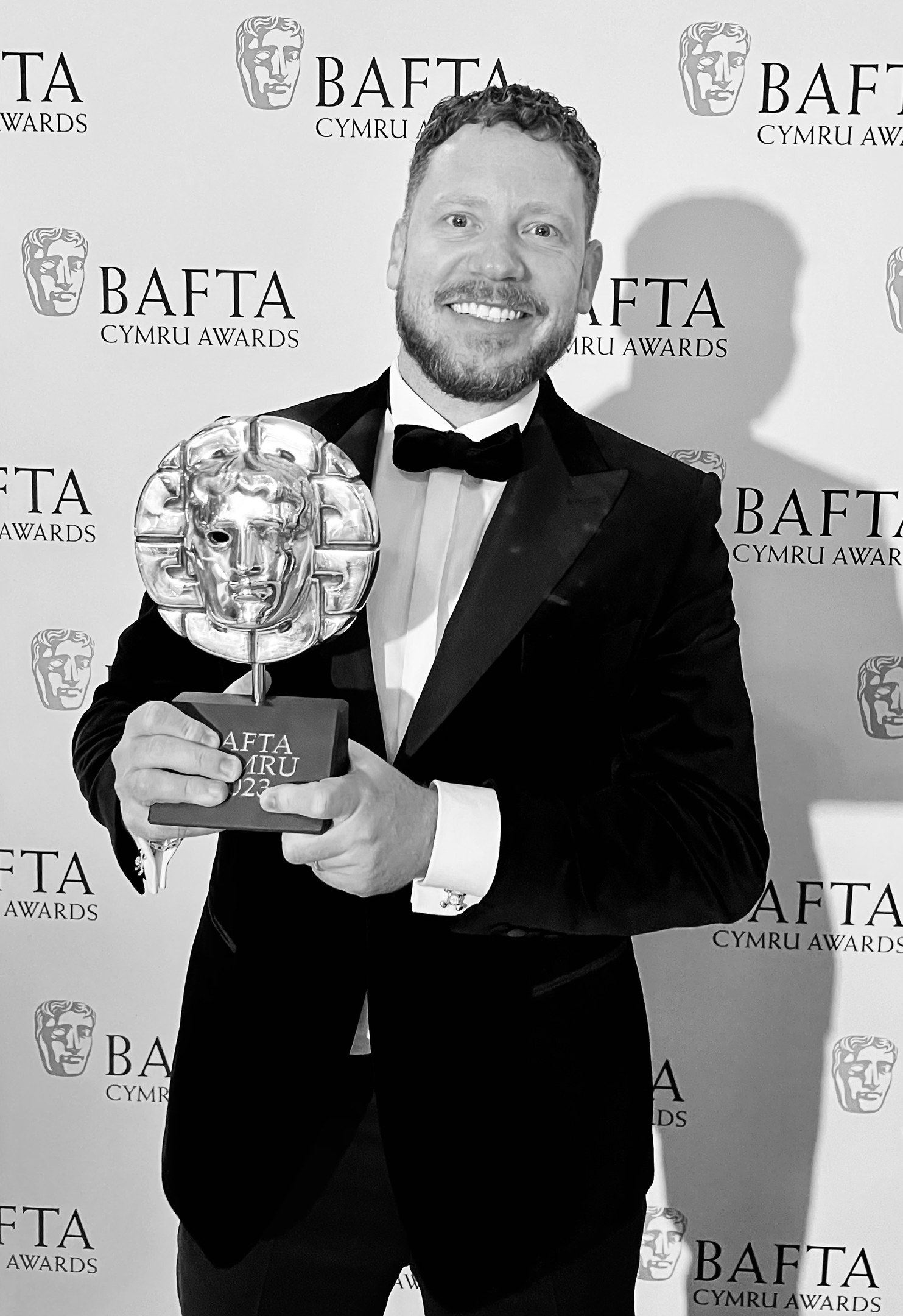 Ein Mann im Smoking mit einem BAFTA-Award, der lächelt, vor einer Hintergrundtafel mit der Aufschrift "BAFTA Awards 2018."