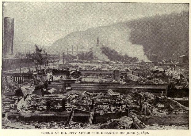 Schwarzes und weißes Foto einer Stadt nach einer Katastrophe am 5. Juni 1892, das Gebäude, Strommäste, Rauch und einen Hügel im Hintergrund zeigt.