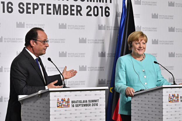 Bundeskanzlerin Angela Merkel und Frankreichs Präsident François Hollande stehen vor zwei Podien mit Mikrofonen, beide lächeln, mit einem Banner im Hintergrund, auf dem "Bratislava Gipfel 2016" steht.