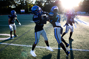 Junge Männer in Helmen und Fußballschuhen auf einem Feld mit Bäumen und einem klaren Himmel.