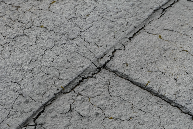 Nahaufnahme einer gebrochenen und verwitterten Straßenoberfläche mit tiefen, breiten Rissen und einer unebenen, rauen Textur.