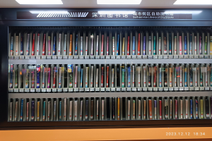 Eine gut beleuchtete Bibliothek mit hohen Bücherregalen voller Bücher, eine Tafel mit Text und ein Wasserzeichen unten, das einer Selbstbedienungsbibliothek in einer städtischen Umgebung ähnelt.