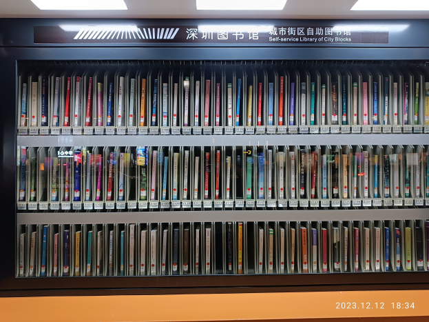 Eine gut beleuchtete Bibliothek mit hohen Bücherregalen voller Bücher, eine Tafel mit Text und ein Wasserzeichen unten, das einer Selbstbedienungsbibliothek in einer städtischen Umgebung ähnelt.