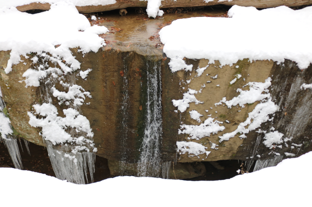 Ein kleiner Wasserfall ergießt sich über eine steile Felswand, die mit unberührtem, reinem Schnee und glitzerndem Eis bedeckt ist und so eine schöne Winterlandschaft schafft.