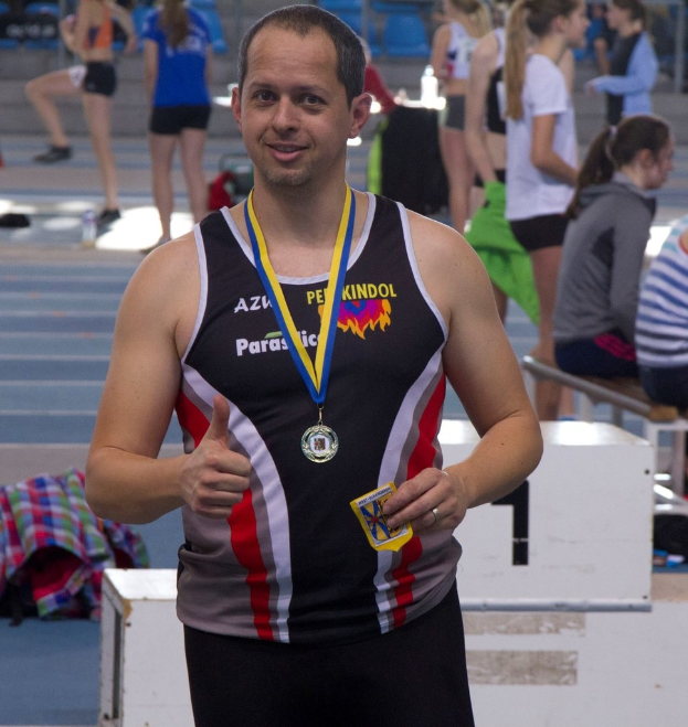 Ein Mann in schwarzem Trikot und Medaille steht vor einer Gruppe von Menschen, die trainieren.