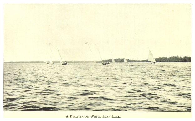 Regatta auf dem Weißen Bärensee mit Booten auf dem Wasser, Bäumen im Hintergrund und Himmel über dem Text unten.
