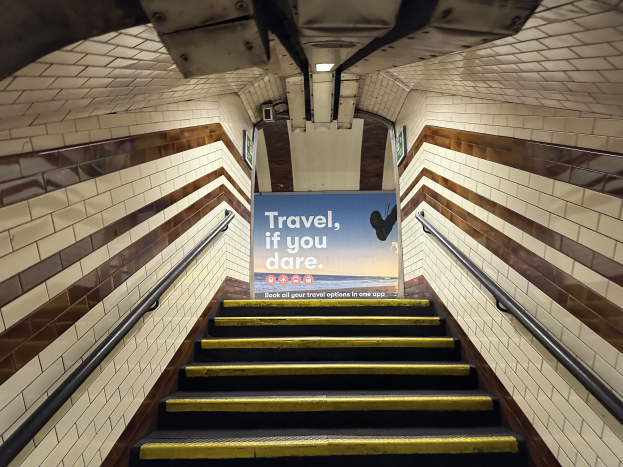 Eine U-Bahn-Stationstreppe mit Geländern auf beiden Seiten, die ein "Reise, wenn du wagst"-Schild oben und sichtbare Stationwände im Hintergrund zeigt.