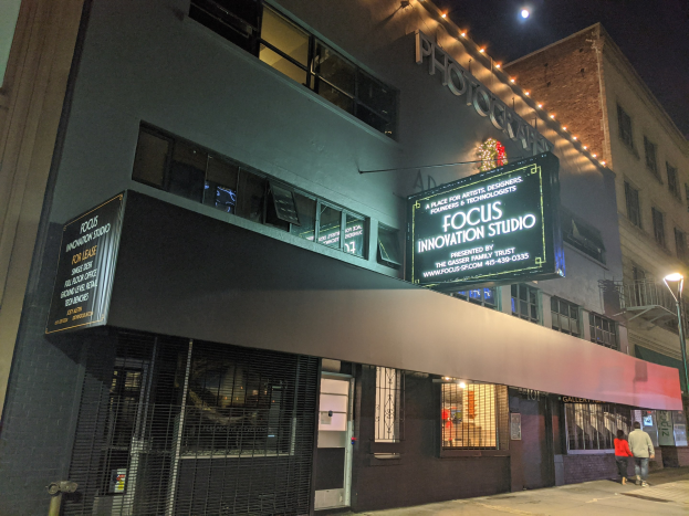 Außenansicht des Focus Innovation Studios in New York City bei Nacht, mit beleuchteten Gebäuden, Menschen auf dem Gehweg und einem sichtbaren Nachthimmel.
