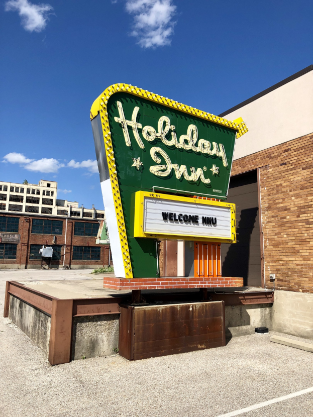 Holiday Inn Schilder an einem Gebäude mit einem Textboard davor, bewölkter Himmel und sichtbare Fenster im Gebäude.