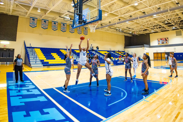 Eine Gruppe von Frauen spielt Basketball in einer Turnhalle mit einem Scoreboard, das ihren NCAA-Turniersieg anzeigt.