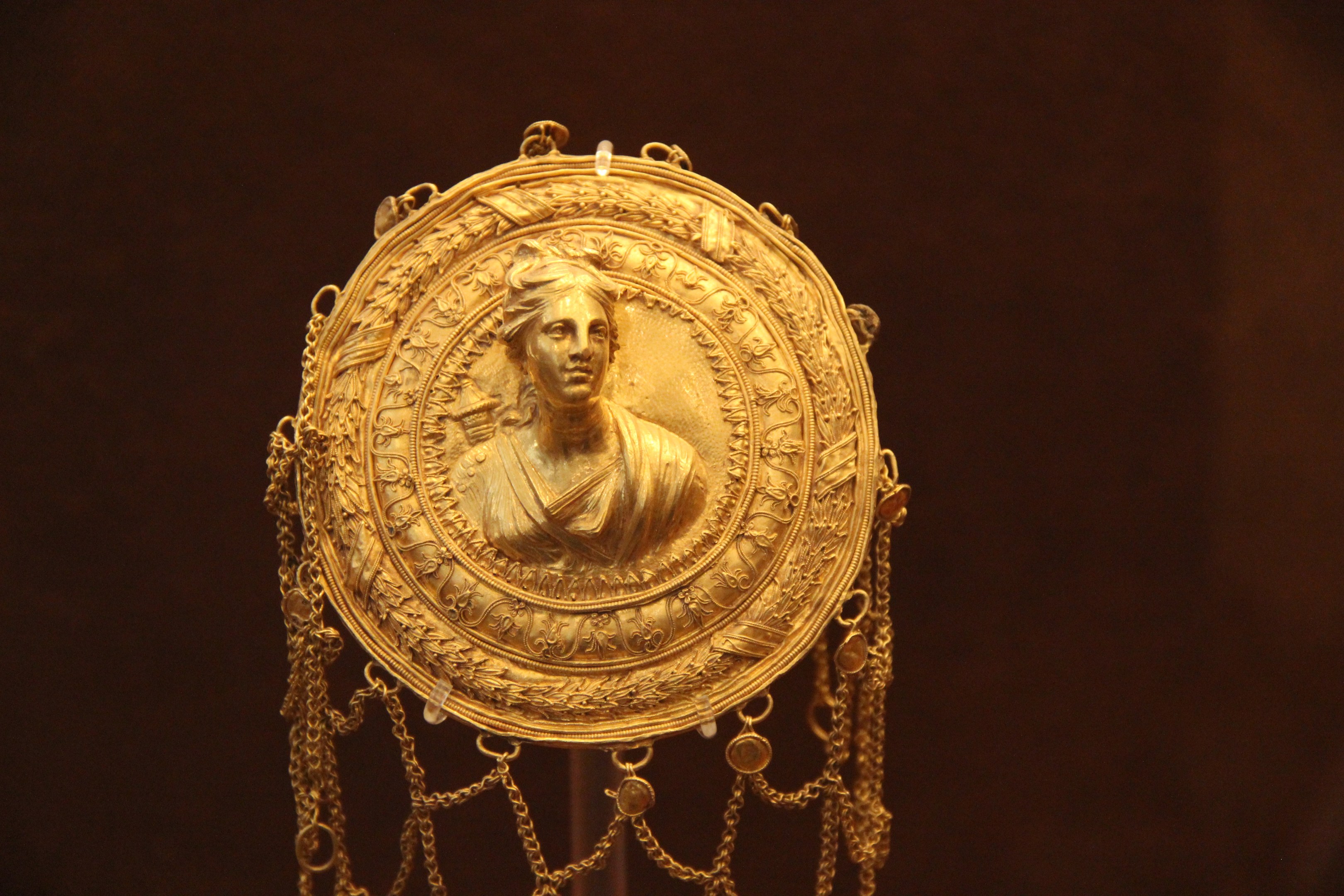 Goldene Medaille mit einer Frauengesicht, vor einem dunklen Hintergrund, mit aufwändigen und luxuriösen Details.