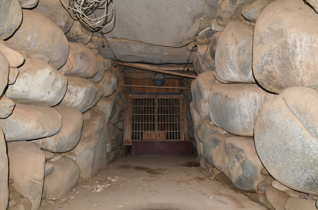 Ein Tunnel voller Steine und ein Metalltor in der Mitte, das an einen Minenschacht mit Drähten oben erinnert.