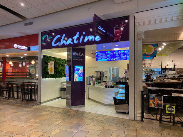 Ein Chatime-Restaurant in einem Einkaufszentrum mit Tischen, Stühlen, Geländern, Texttafeln, Bildschirmen und Lichtern, das den Boden unten zeigt.
