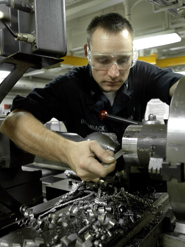 Ein Fräser mit Schutzbrille bedient eine Maschine in einer gut beleuchteten Fabrikumgebung.