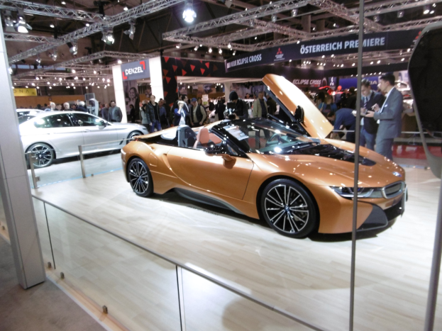 Ein schickes schwarzes BMW i8 Cabrio mit Chromakzenten, langer Haube und niedriger Karosserie, umgeben von formell gekleideten G├Ąsten auf der Frankfurter Motor Show.