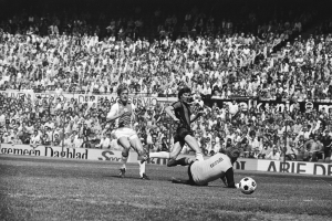 Schwarzes Foto von Fussballspielern im Einsatz auf einem Feld mit Zuschauern im Hintergrund und einem Banner mit der Aufschrift "Bundesliga 1978-79 Ajax 1-1 Hannover 96."
